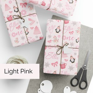 May include: Pink wrapping paper with a repeating pattern of penguins, snowmen, and hot chocolate mugs. The name "Ellie" is repeated throughout the design.