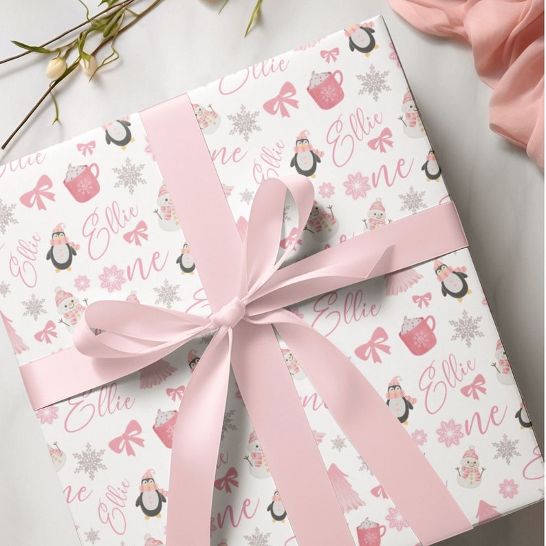 May include: Pink and white wrapping paper with a repeating pattern of penguins, snowflakes, and the name "Ellie".