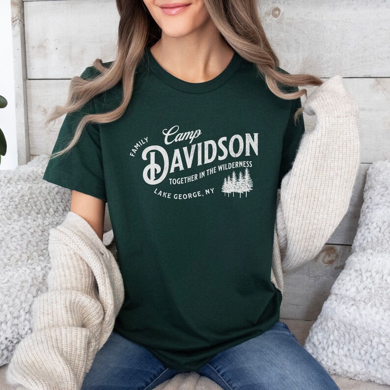 May include: A dark green t-shirt with a white vintage-style graphic that says "Camp Davidson Family Together in the Wilderness Lake George, NY".