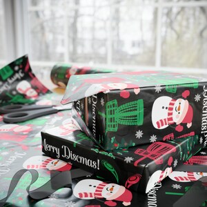Może przedstawiać: Stos trzech pudełek prezentowych owiniętych w czarno-zielony papier ozdobny z motywem bałwana i kosza do frisbee. Pudełka są oznaczone napisami "Merry Discmas!" i "Discmas!"