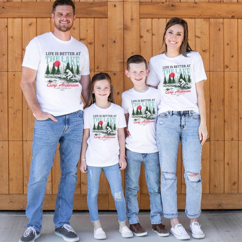 K&ouml;nnte beinhalten: Vier wei&szlig;e T-Shirts mit einer Grafik aus Wald, roter Sonne und B&auml;r sowie dem Text "LIFE IS BETTER AT THE LAKE", "Camp Anderson" und "LAKE TAHOE, CA 2023". Die T-Shirts werden mit blauen Jeans in verschiedenen Ausf&uuml;hrungen kombiniert.