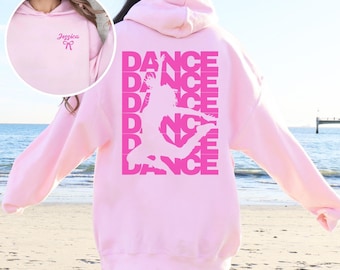 May include: A light pink hooded sweatshirt featuring a large dark pink graphic on the back with the word DANCE repeated six times and a silhouette of a dancer. The front chest area displays the name Jessica above a small bow icon.