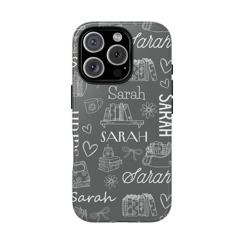 May include: A gray phone case with a white pattern of books, flowers, hearts, bows, and the name "Sarah" repeated throughout. The case has a glossy finish and a camera cutout.