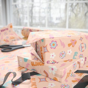 May include: Two gift boxes wrapped in pink and orange wrapping paper with a retro pattern of flowers, mushrooms, and rainbows. The boxes are stacked on top of each other and the top box has the name "Oliver" written on it.