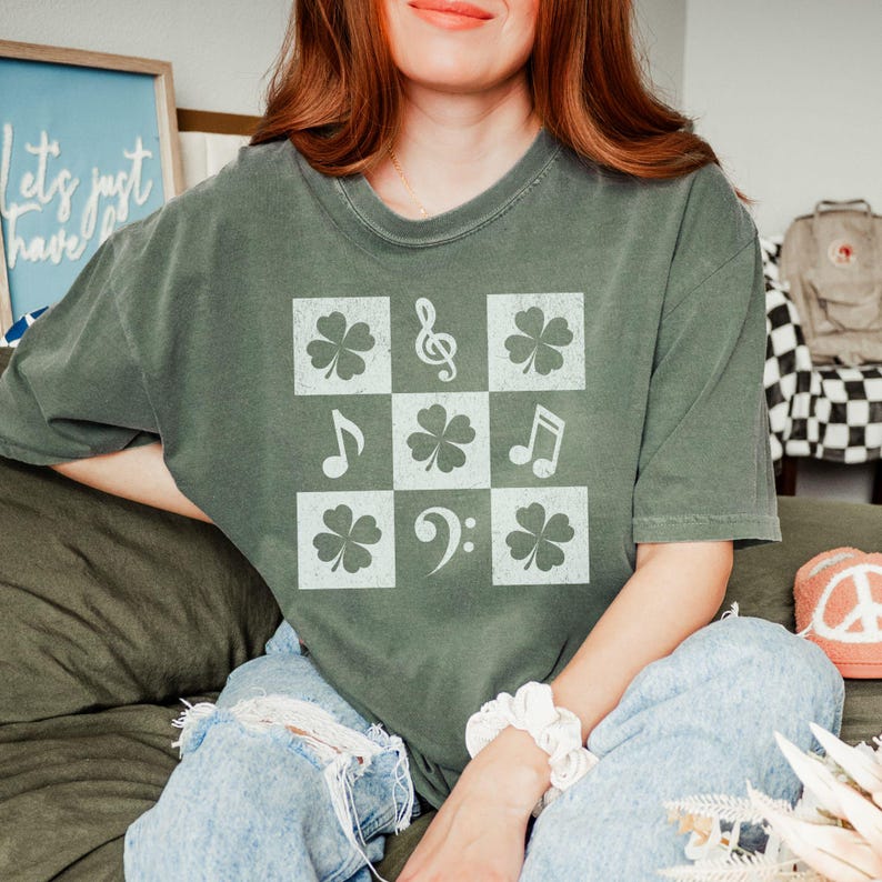 May include: A green t-shirt with a white design of four-leaf clovers, musical notes, and a treble clef.