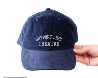 May include: A navy blue corduroy baseball cap featuring the embroidered text SUPPORT LIVE THEATRE in white capital letters on the front panel. The cap has a structured crown, a curved brim, and matching navy blue eyelets.