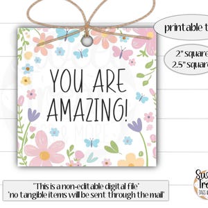 Op de afbeelding: Printbare tag met een bloemenontwerp en de tekst "YOU ARE AMAZING!" in zwart. De tag is verkrijgbaar in twee maten: 2 inch vierkant en 2,5 inch vierkant.