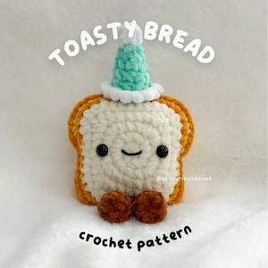 May include: A crocheted plush of a slice of toast with a smiling face, wearing a teal party hat. The text "TOASTY BREAD" and "crochet pattern" are above and below the plush. The plush has brown feet.