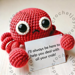 May include: A red crocheted crab with white eyes and a sad expression holds a white card with the text "I'll always be here to help you deal with all your crab!"