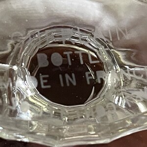 May include: Close-up of a clear glass bottle base with the text "BOTTLE MADE IN FRANCE" etched into the glass. The bottle has a unique, faceted design.