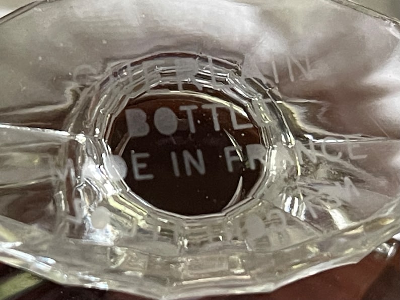May include: Close-up of a clear glass bottle base with the text "BOTTLE MADE IN FRANCE" etched into the glass. The bottle has a unique, faceted design.