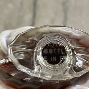 May include: Close-up of a clear, faceted perfume bottle with a brown liquid inside. The bottle has a geometric design and the text "BOTTLE MADE IN FRANCE" is visible. The bottle is likely vintage.