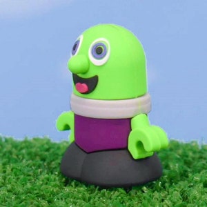 May include: A green and purple toy figure with a large nose and big eyes. The figure is wearing a white and purple outfit and has a black base.