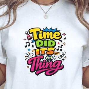 Peut inclure: T-shirt blanc avec un motif coloré « Time Did Its Thing ». Le design comprend un chapeau de fête, des notes de musique, des étoiles et une boule disco. Le t-shirt est de style col rond.