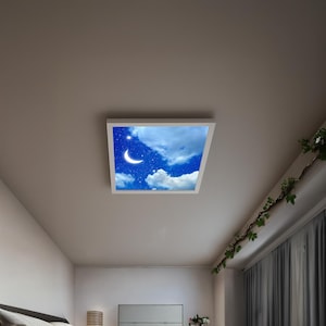 May include: A square ceiling light fixture with a white frame. The light panel displays a nighttime sky scene with a crescent moon, stars, and fluffy white clouds against a blue background. The fixture is mounted on a white ceiling.