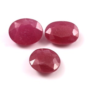 Può includere: Tre rubini ovali sfaccettati di diverse dimensioni sono presentati su sfondo bianco. Le pietre preziose, di un rosso intenso, presentano molteplici sfaccettature che catturano la luce, creando un effetto scintillante. Adatto per la gioielleria.