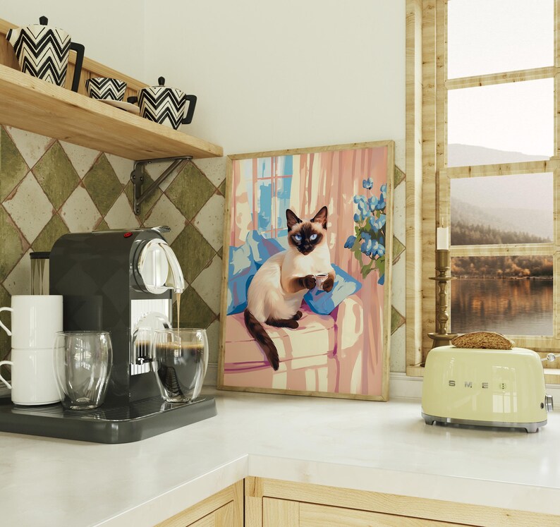 May include: A kitchen scene featuring a black espresso machine dispensing coffee into a glass. A framed painting of a Siamese cat on a couch is visible. A light green toaster sits on the counter, with a slice of toast.