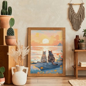 May include: A framed painting of two cats sitting on a rock by the ocean at sunset. The cats are looking out at the water. The painting is in a wooden frame and has a light brown background.