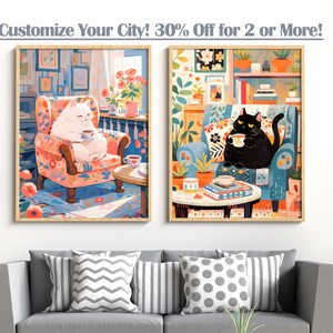 May include: Two framed illustrations of cats sitting in armchairs, each holding a cup. The cat on the left is white and the cat on the right is black. Both cats are sitting in floral patterned armchairs. The illustrations are set against a white wall.