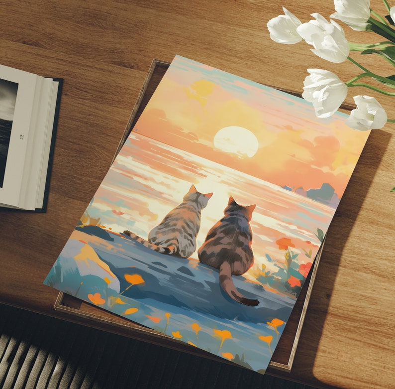 May include: Two gray tabby cats sit side-by-side on a rocky shore, looking out at a sunset over a body of water. The sky is a vibrant orange and pink, with a large sun setting in the distance.
