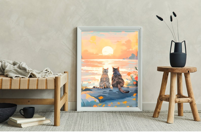 May include: A framed painting of two cats sitting on a rock by the ocean, watching the sunset. The sky is a vibrant orange and pink, and the water is a calm blue. The cats are facing away from the viewer, and their tails are curled around their bodies.