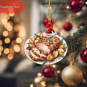May include: A Christmas tree ornament featuring a festive plate of roasted meat, potatoes, and apples. The ornament has a Santa hat with the name "Ann" and the words "Custom Text" above. The ornament is hanging on a Christmas tree with red and gold ornaments.