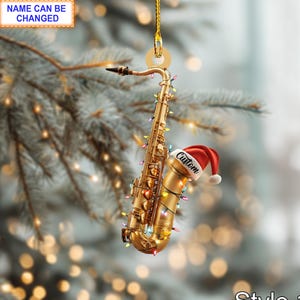Peut inclure: Ornement de Noël en forme de saxophone doré, orné d'un chapeau de Père Noël rouge avec l'inscription "Custom". Le saxophone est décoré de lumières colorées et suspendu à un fil doré. Le texte "NAME CAN BE CHANGED" est dans un encadré blanc. Le texte "Style 1" est en bas.