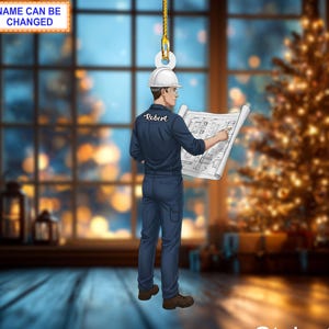May include: Ornament featuring an engineer in a navy blue jumpsuit and white hard hat, holding a blueprint. The ornament is suspended by a gold chain. Text on the ornament reads "Name Can Be Changed" and "Robert". The style is labeled "Style 1".