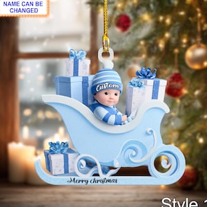 Può includere: Un ornamento natalizio blu raffigurante un bambino su una slitta con regali confezionati. L'ornamento ha il testo "Merry Christmas" e "Custom". È appeso a un filo d'oro.