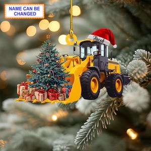 May include: A yellow toy construction vehicle with a Christmas tree and presents in the bucket. The vehicle has a red Santa hat on the cab with the name "Jacob" written on it.