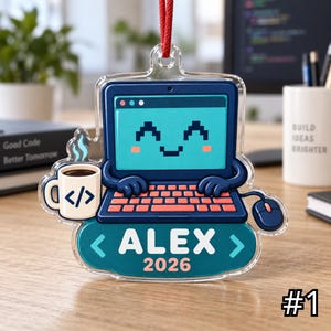 Op de afbeelding: Een hangend ornament van doorzichtig acryl met een cartoonlaptop met een lachend pixelgezicht, een koffiemok met een codesymbool en een computermuis. Het ontwerp bevat de naam ALEX en het jaar 2026 in witte tekst op een donkerblauwe achtergrond.