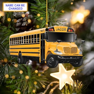 Può includere: Un ornamento a forma di autobus scolastico giallo con il nome "JACOB" sul davanti. L'ornamento è appeso a un filo dorato e si trova davanti a un albero di Natale.