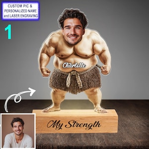 May include: A custom-made wooden figurine of a person with a large, muscular build. The figurine is wearing a brown loincloth and has a name, "Charlotte", written on the front. The base of the figurine is made of wood and has the words "My Strength" engraved on it.