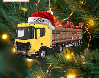 May include: Yellow and red Christmas ornament featuring a personalized log truck hauling logs. The truck has a Santa hat with the name "Eddy" on it.