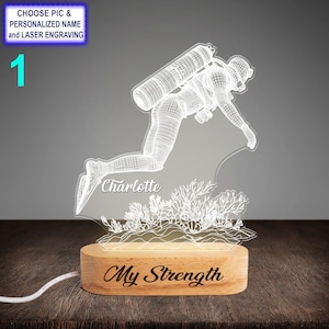 Könnte beinhalten: Ein weißes, 3D-gedrucktes Nachtlicht, das einen Taucher mit Tank und Flossen darstellt. Der Sockel des Lichts ist aus Holz und trägt die Worte "My Strength" eingraviert. Der Name "Charlotte" ist ebenfalls in den Sockel eingraviert.