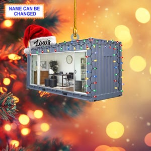Könnte beinhalten: Grauer, containerförmiger Weihnachtsschmuck mit einer Miniatur-Büroszene, die durch die Glastüren sichtbar ist. Der Schmuck ist mit einem Weihnachtsmannhut und Lichterketten verziert. Der Text "NAME CAN BE CHANGED" und "Louis" ist sichtbar.