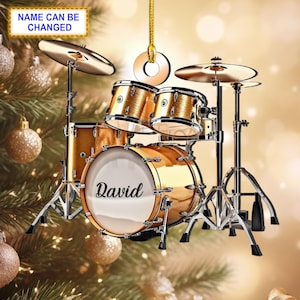May include: Gold-coloured drum set ornament with the name "David" on the bass drum. The ornament is hanging from a gold string and is ideal for a drummer or music lover.