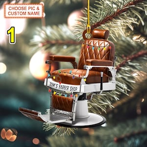 Puede incluir: Una silla de barbero de cuero marrón con una base blanca y detalles cromados. La silla tiene un letrero que dice "Tom's Barber Shop" y está decorada con luces de colores. La silla está colgada de una cuerda dorada, lo que sugiere que es un adorno navideño.