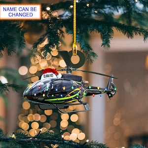 May include: A black helicopter ornament with a Santa hat that says "DAVID" on it. The helicopter has colorful lights strung around it and is hanging from a Christmas tree.