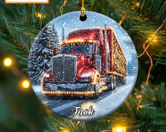 May include: A red semi-truck with a Christmas tree trailer drives through a snowy winter scene. The truck is decorated with lights and the trailer is covered in Christmas ornaments. The ornament is personalized with the name "Fack".