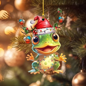 May include: A green Christmas ornament shaped like a frog wearing a Santa hat and reindeer antlers. The frog is decorated with colorful lights and is smiling.