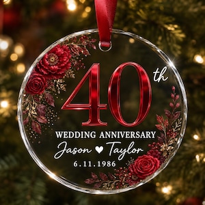 May include: A round clear glass ornament featuring a red ribbon hanger. The design includes the text 40th WEDDING ANNIVERSARY, the names Jason and Taylor separated by a heart, and the date 6.11.1986, accented with deep red floral illustrations.