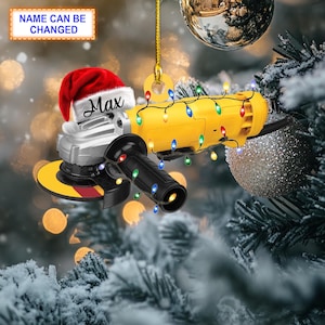 Puede incluir: Una amoladora angular amarilla y plateada con un gorro de Papá Noel rojo en la parte superior. La amoladora está decorada con una cadena de luces navideñas de colores. El texto "Max" está escrito en el gorro de Papá Noel.