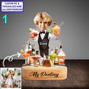 May include: A personalized acrylic night light featuring a cartoon illustration of a person holding a cocktail. The base of the light is made of wood and has the text "My Destiny" engraved on it. The person in the illustration is wearing a black vest and bow tie and has the name "Louis" written on their vest.