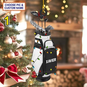 May include: A white and black golf bag with a string of colorful Christmas lights wrapped around it. The bag is filled with golf clubs and has the name "XAVIER" printed on the side.