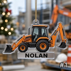 May include: A clear acrylic hanging ornament shaped like an orange and black backhoe loader construction vehicle. The design features a detailed side profile of the machinery with a rectangular base plate at the bottom displaying the name NOLAN.