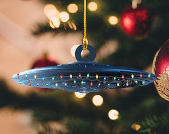 May include: A dark blue UFO Christmas ornament with a string of colorful lights around the edge. The ornament is hanging from a gold string.