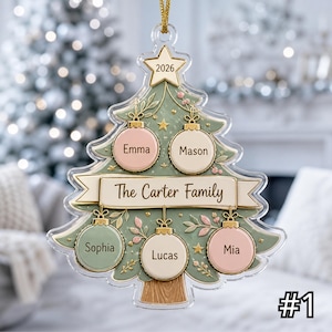 Könnte beinhalten: Ein transparenter Acryl-Weihnachtsbaumschmuck mit einem salbeigrünen Baumdesign und einem goldenen Stern an der Spitze mit der Aufschrift 2026. Er enthält ein zentrales Banner mit der Aufschrift The Carter Family und fünf runde Anhänger mit den Namen Emma, Mason, Sophia, Lucas und Mia.