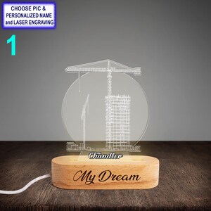 May include: A white acrylic 3D night light with a design of a construction crane and building. The base is made of wood and has the words "Chandler" and "My Dream" engraved on it.