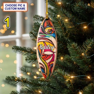May include: A colorful surfboard ornament with a white background and the name "Bailey" written in white letters. The ornament is hanging from a Christmas tree.